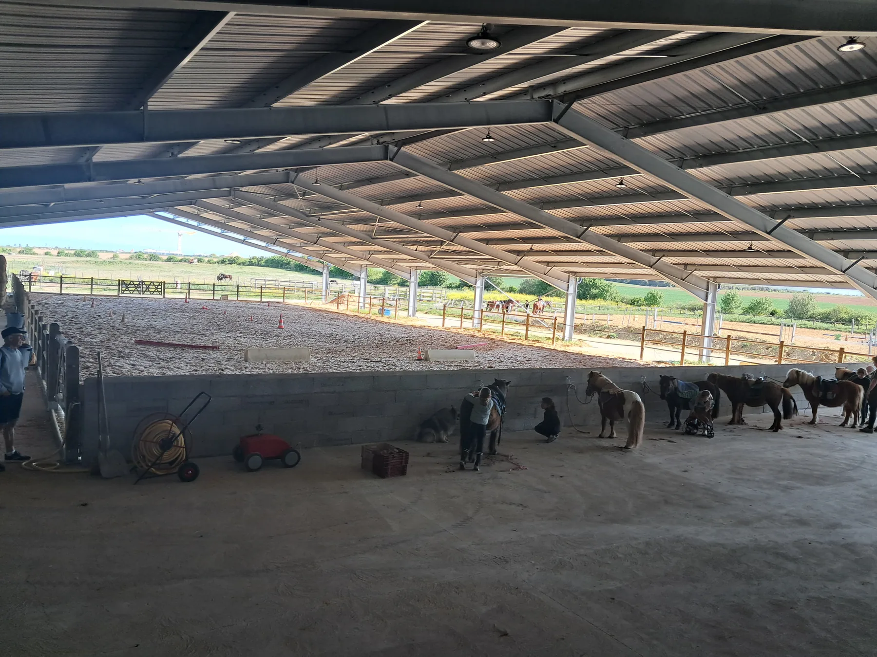 Sous le manège couvert, des poneys sellés attendent le cours, les plaines au fond